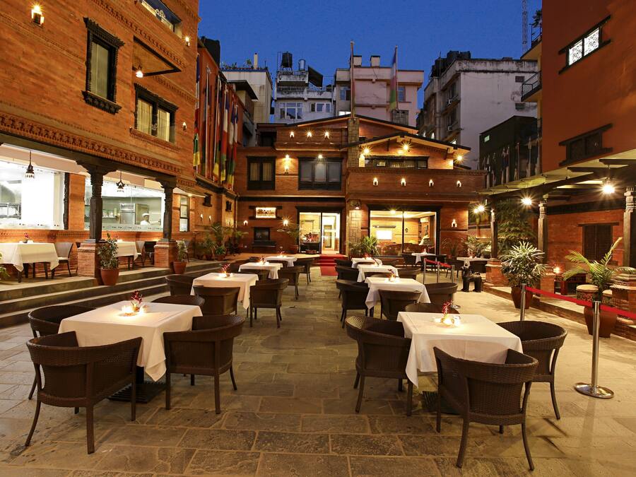 An outdoor dining area with tables and chairs, surrounded by buildings with brick facades and multiple windows.