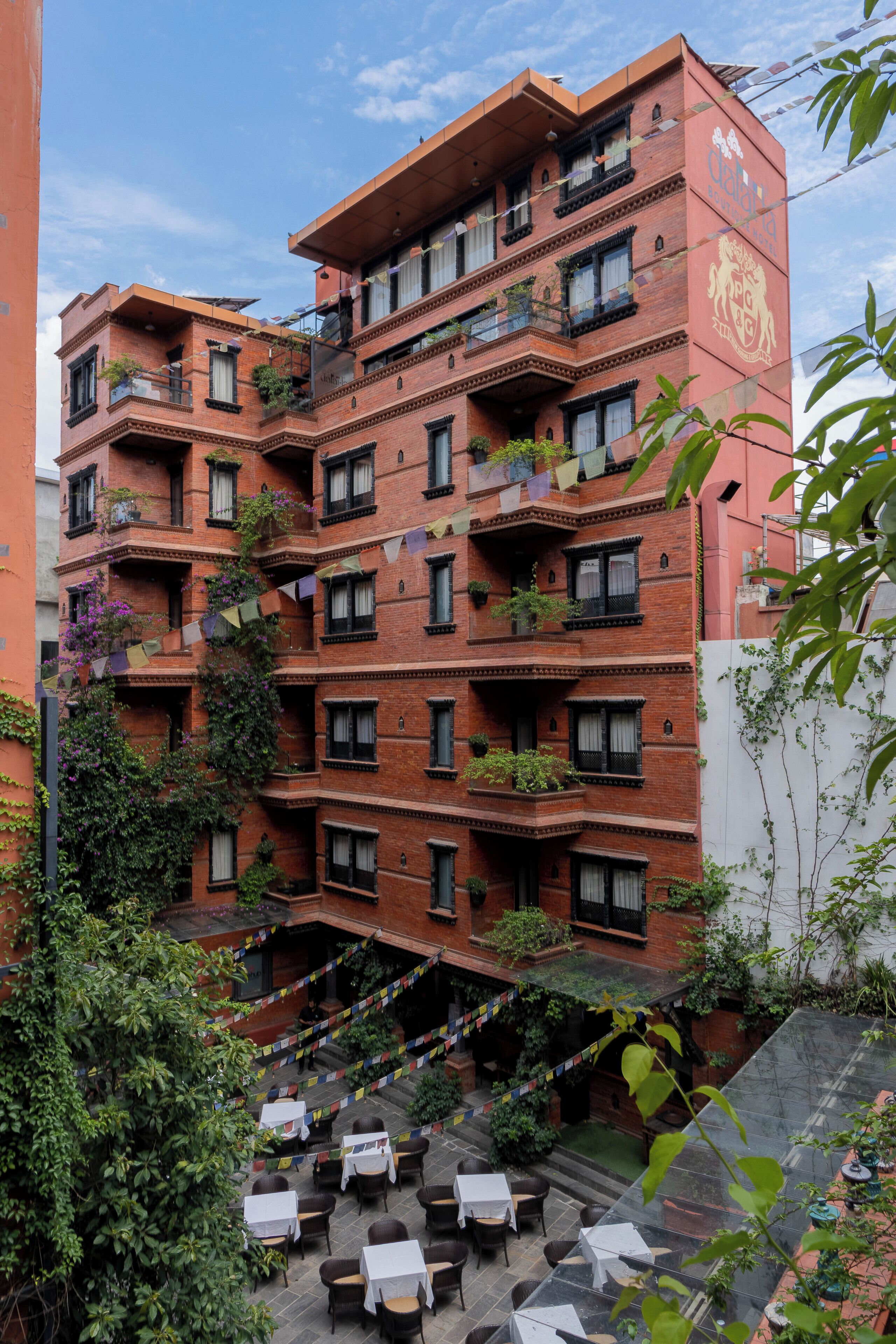 A multi-story brick building with balconies, outdoor seating, and greenery.