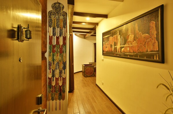 A hallway with a wooden door, a decorative hanging, and a framed painting on the wall.