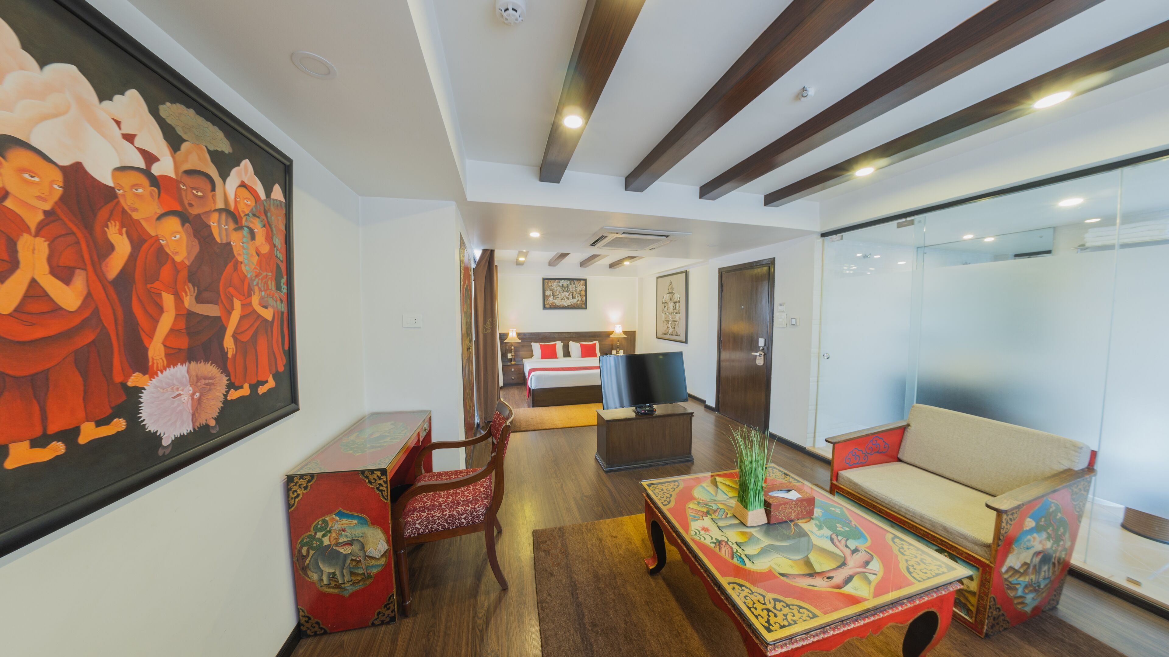 A hotel room with a bed, a TV, a sofa, a desk, and a painting on the wall.