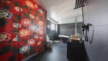 A modern bathroom with a red floral wall, a toilet, a sink with a mirror, and a telephone mounted on the wall.