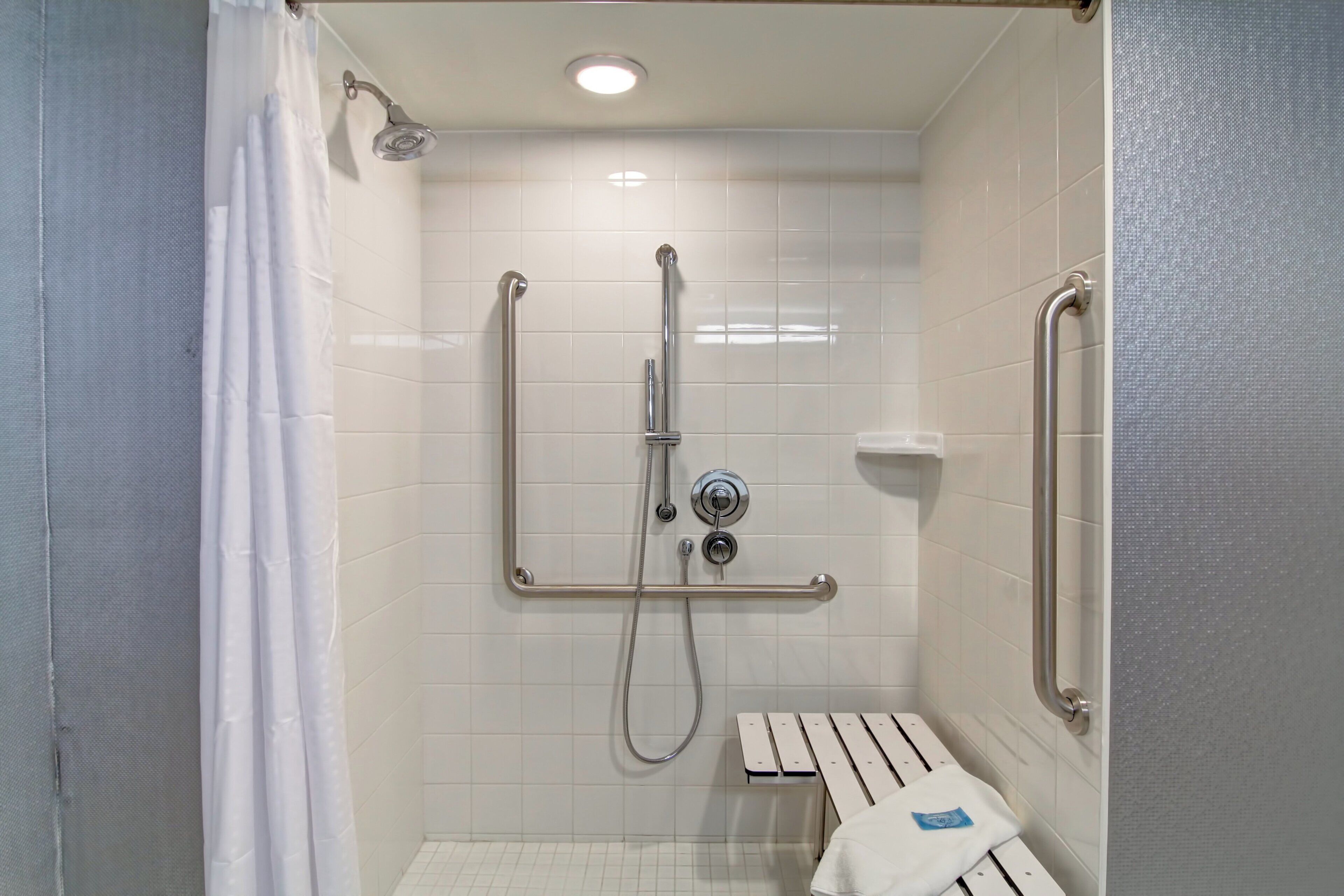 A shower with grab bars, a bench, and a handheld showerhead.