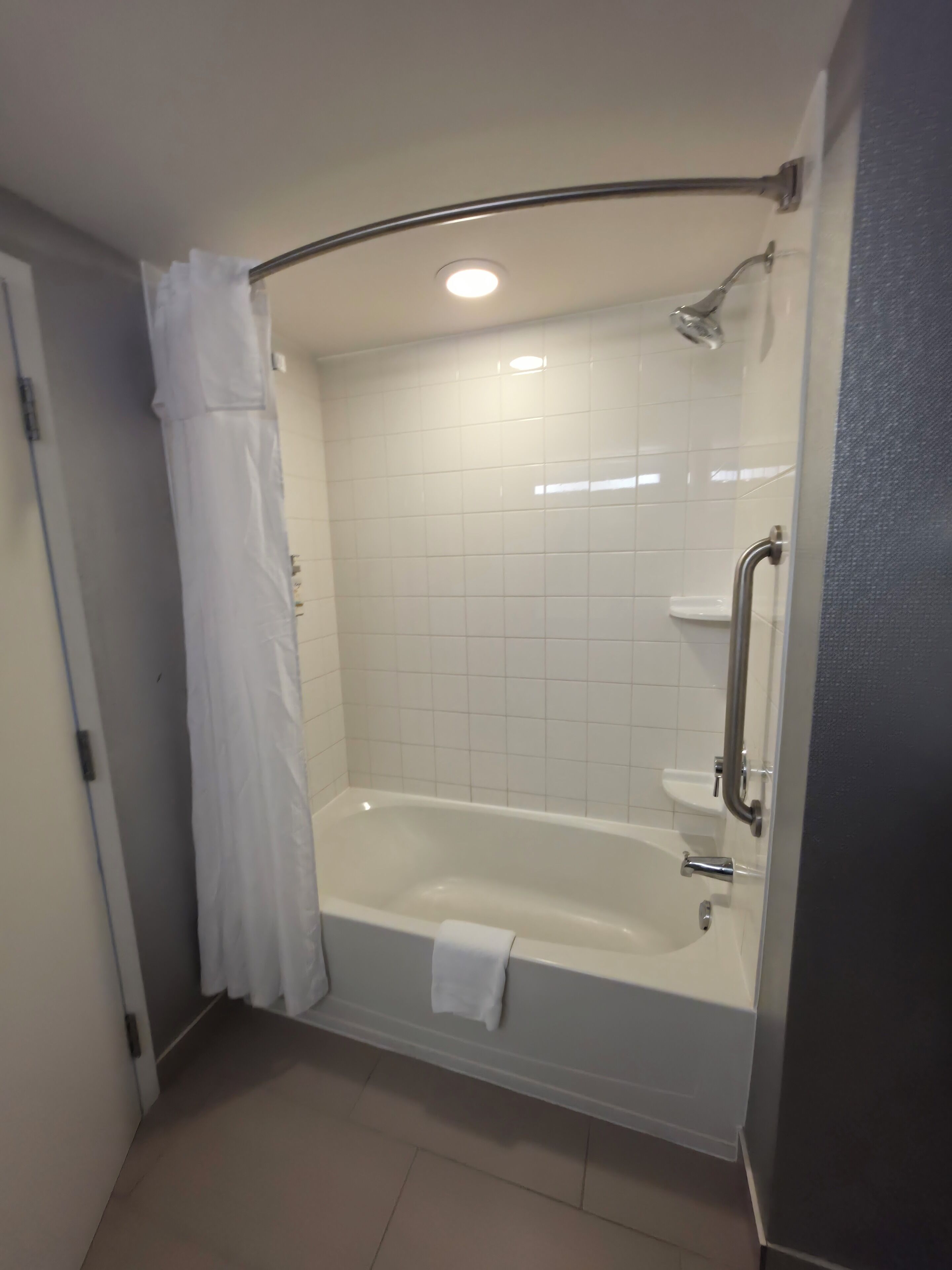 Un baño con bañera, ducha, barandilla y cortina blanca.