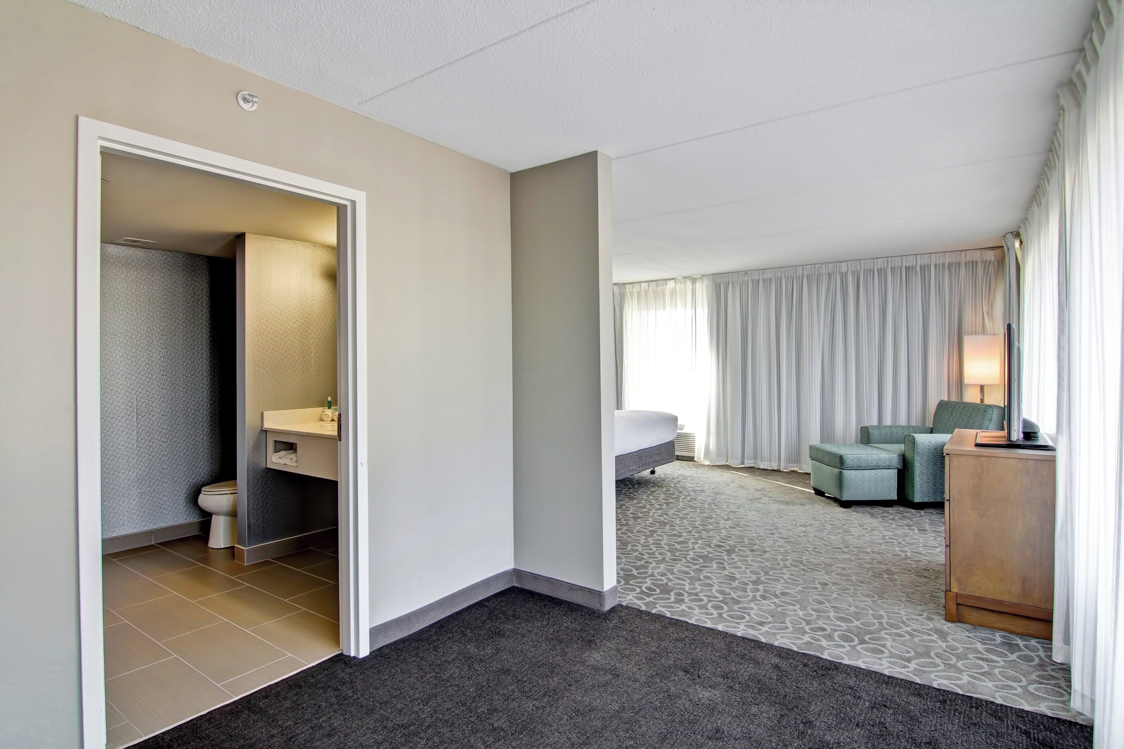 A hotel room with a bathroom, a bed, a sofa, and a desk.