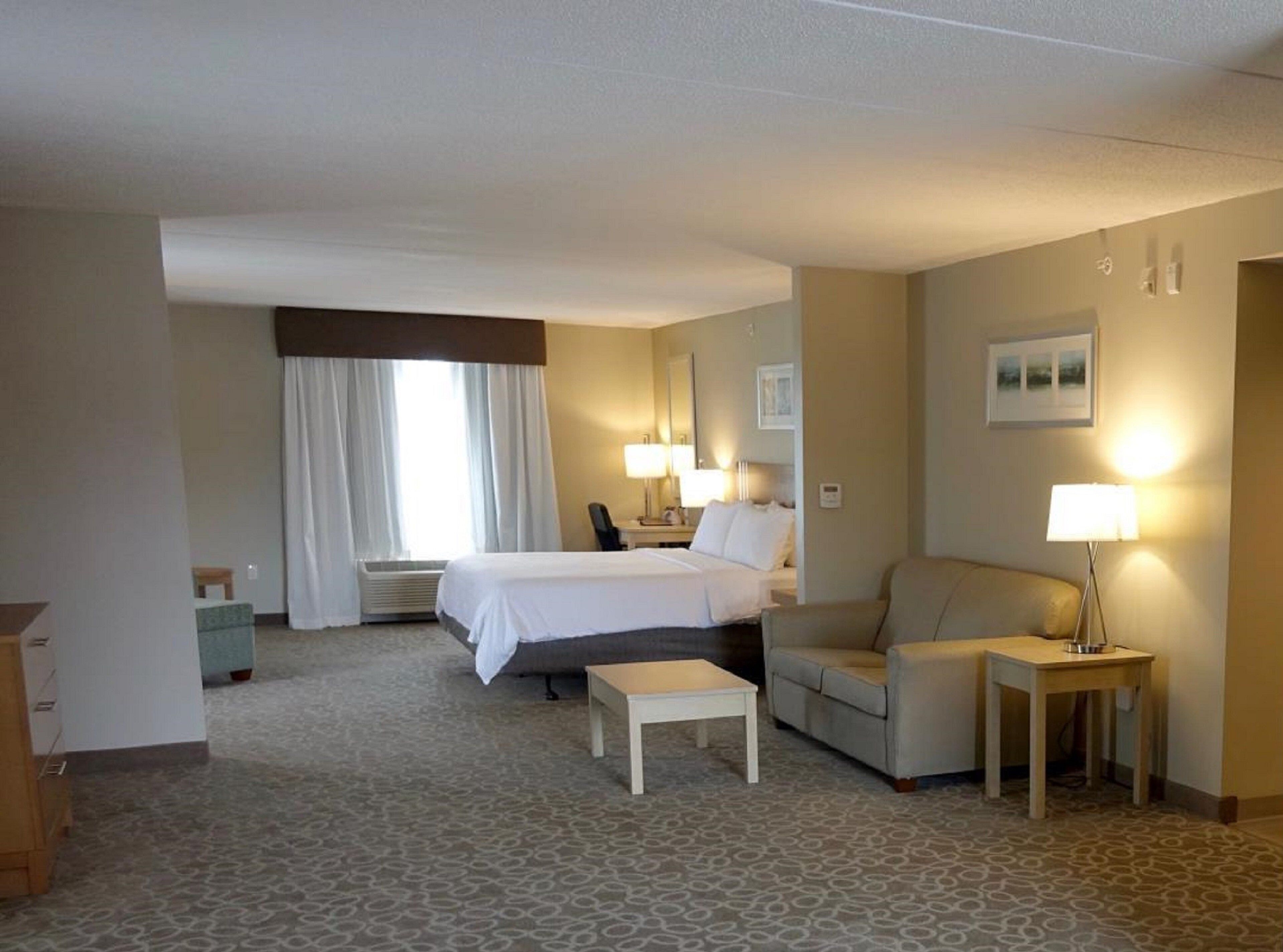 Una habitación de hotel con cama, sofá, una mesita, lámpara y un cuadro en la pared.