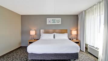 A hotel room with a large bed, two bedside lamps, a framed artwork above the bed, and a window with curtains.