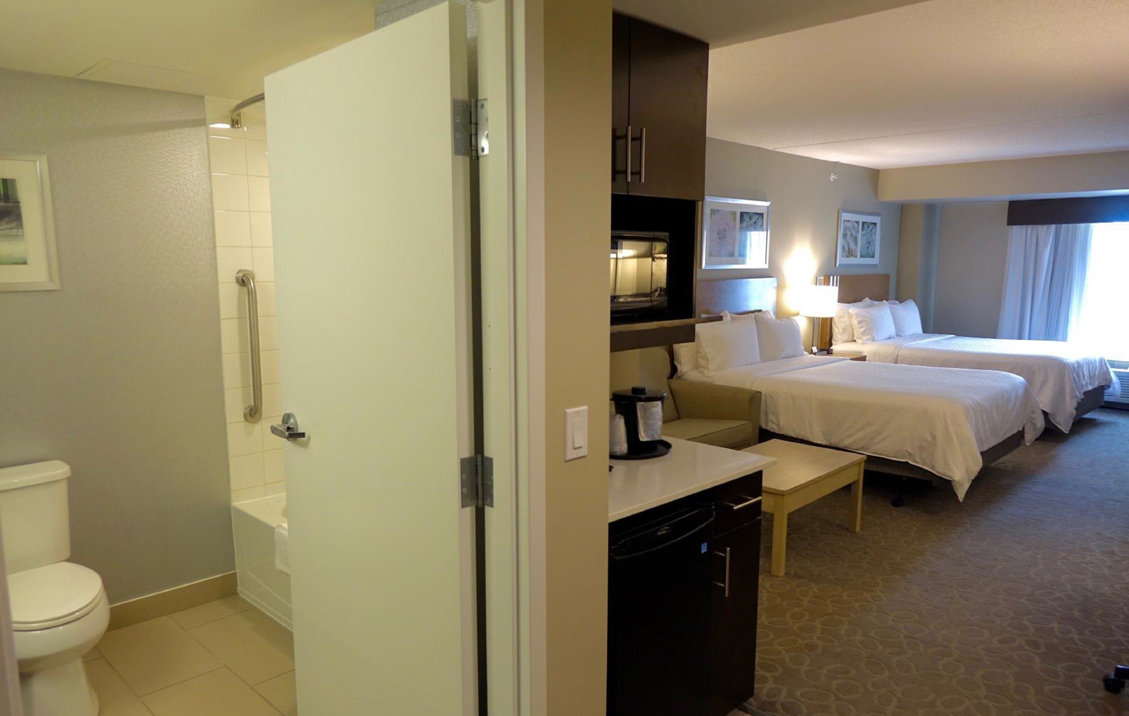 A hotel room with a bathroom, a kitchenette, and two beds.