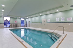 An indoor swimming pool with a shallow water area marked, a changing room, and a seating area with tables and chairs.