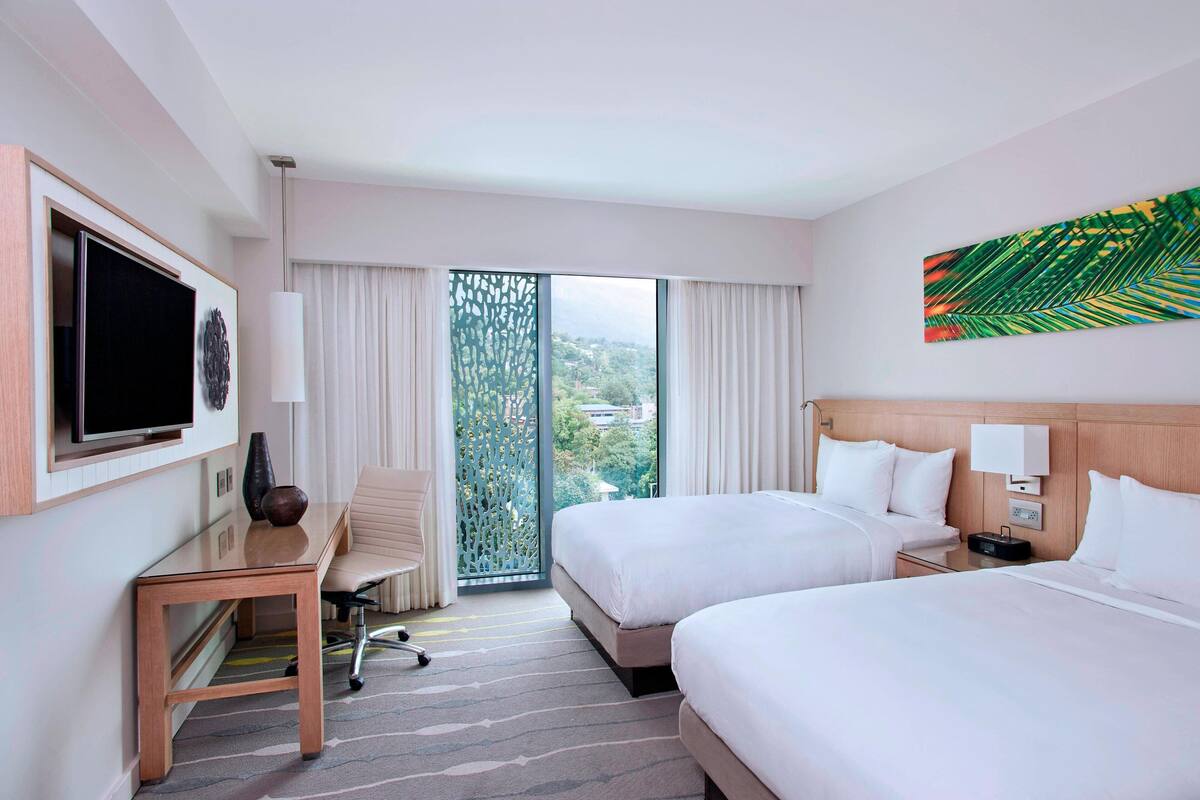 Een hotelkamer met twee bedden, een televisie, een bureau en een groot raam met uitzicht.