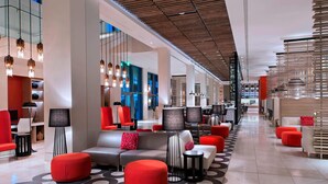 A modern hotel lobby with a central seating area, a staircase, and a view of the city.