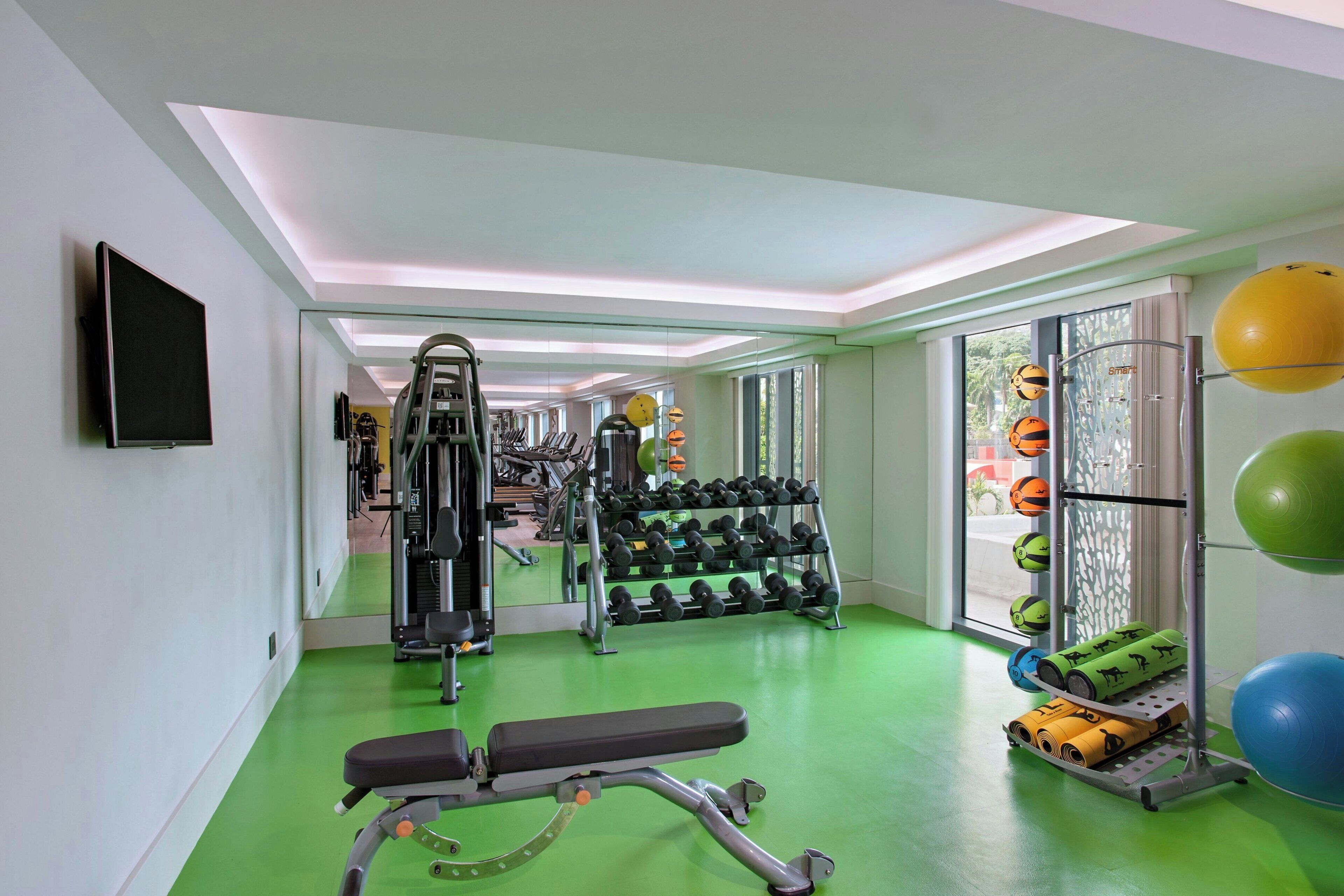 A gym with exercise equipment, a bench, dumbbells, and exercise balls.