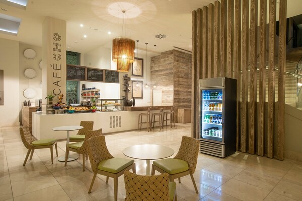 A modern café interior with a central counter, seating area, and a beverage refrigerator. - Marriott Port-au-Prince Hotel (Port-au-Prince)