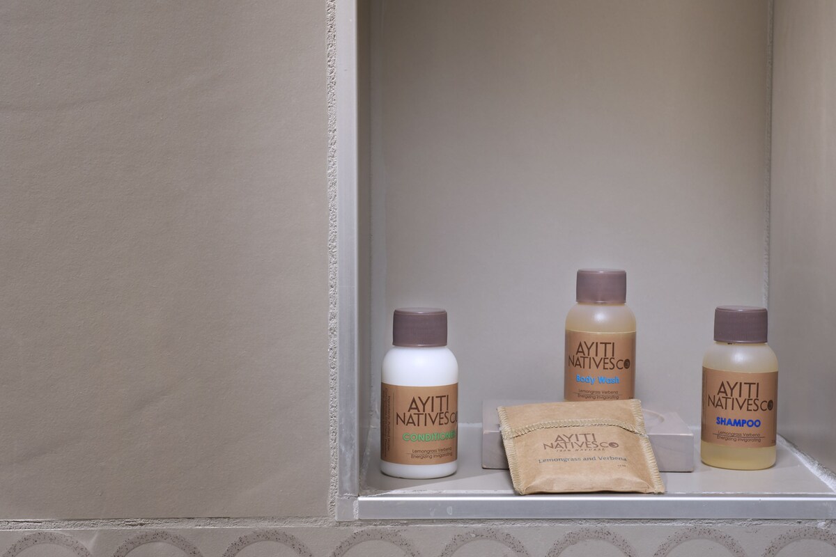 A bathroom shelf with three bottles of Ayiti Nativesco body wash and shampoo, and a bar of soap.