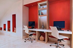 A modern office with two desks, each with a computer monitor, white chairs, and a bookshelf with books and decorative items. - Marriott Port-au-Prince Hotel (Port-au-Prince)
