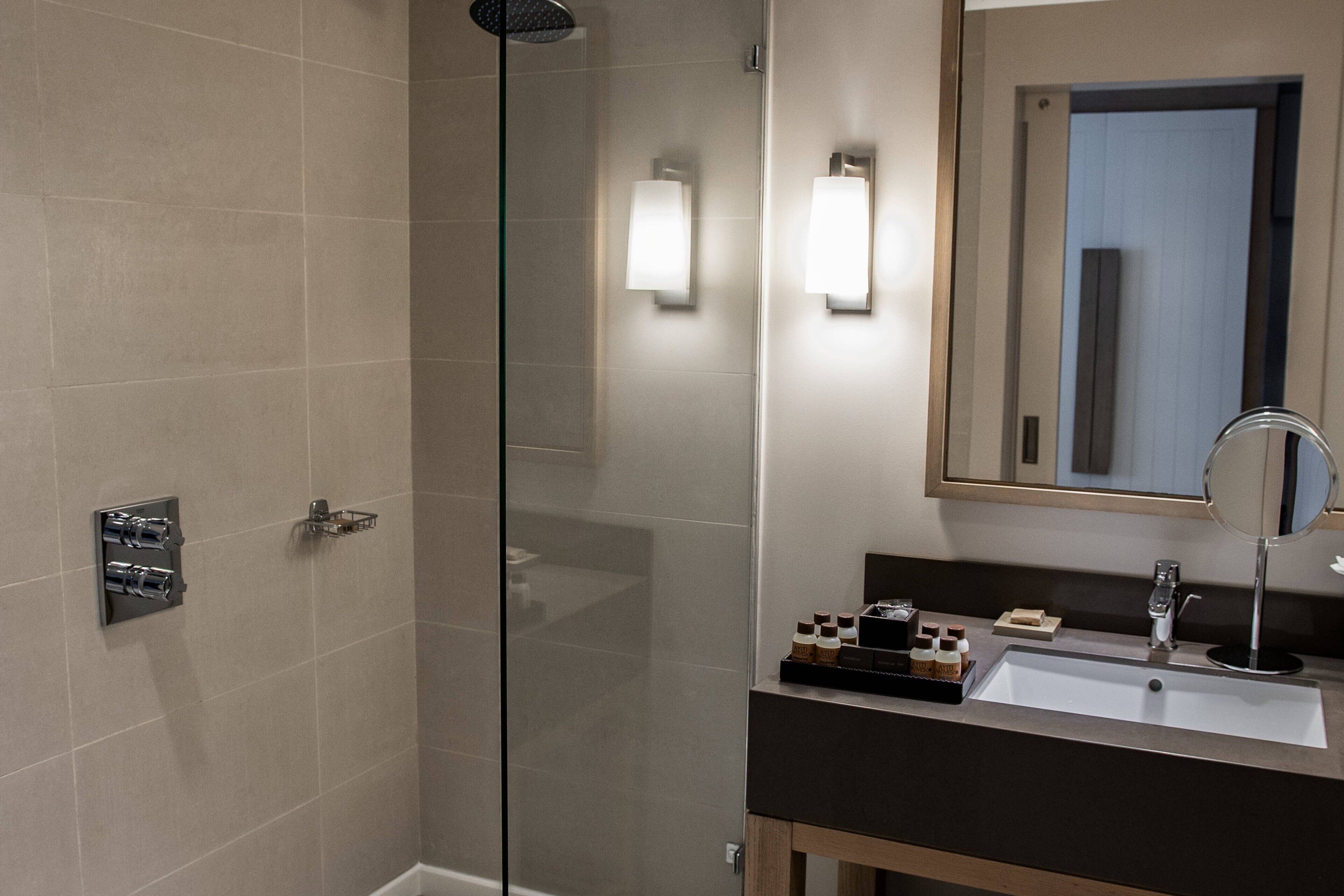 A modern bathroom with a glass shower enclosure, a sink with a mirror, and wall-mounted lighting.