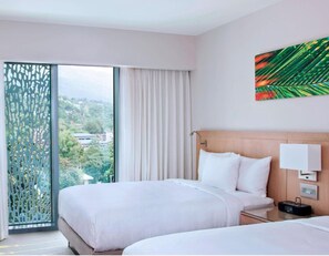 A hotel room with two beds, a view through a large window, a curtain, a wall-mounted lamp, and a painting. - Marriott Port-au-Prince Hotel (Port-au-Prince)