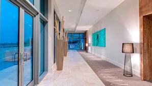 A modern hotel corridor with glass doors, a long hallway, and a view of the outside.