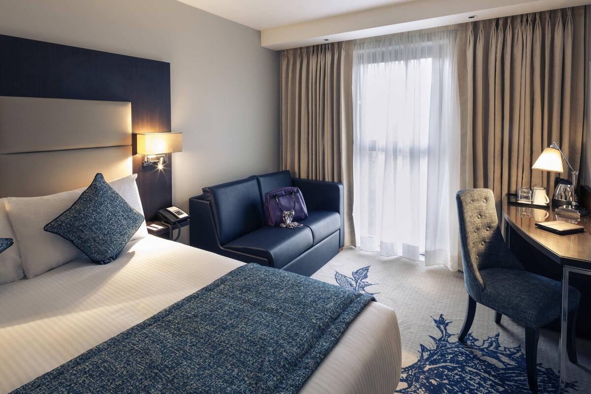 A hotel room with a bed, a sofa, a desk, and a chair.