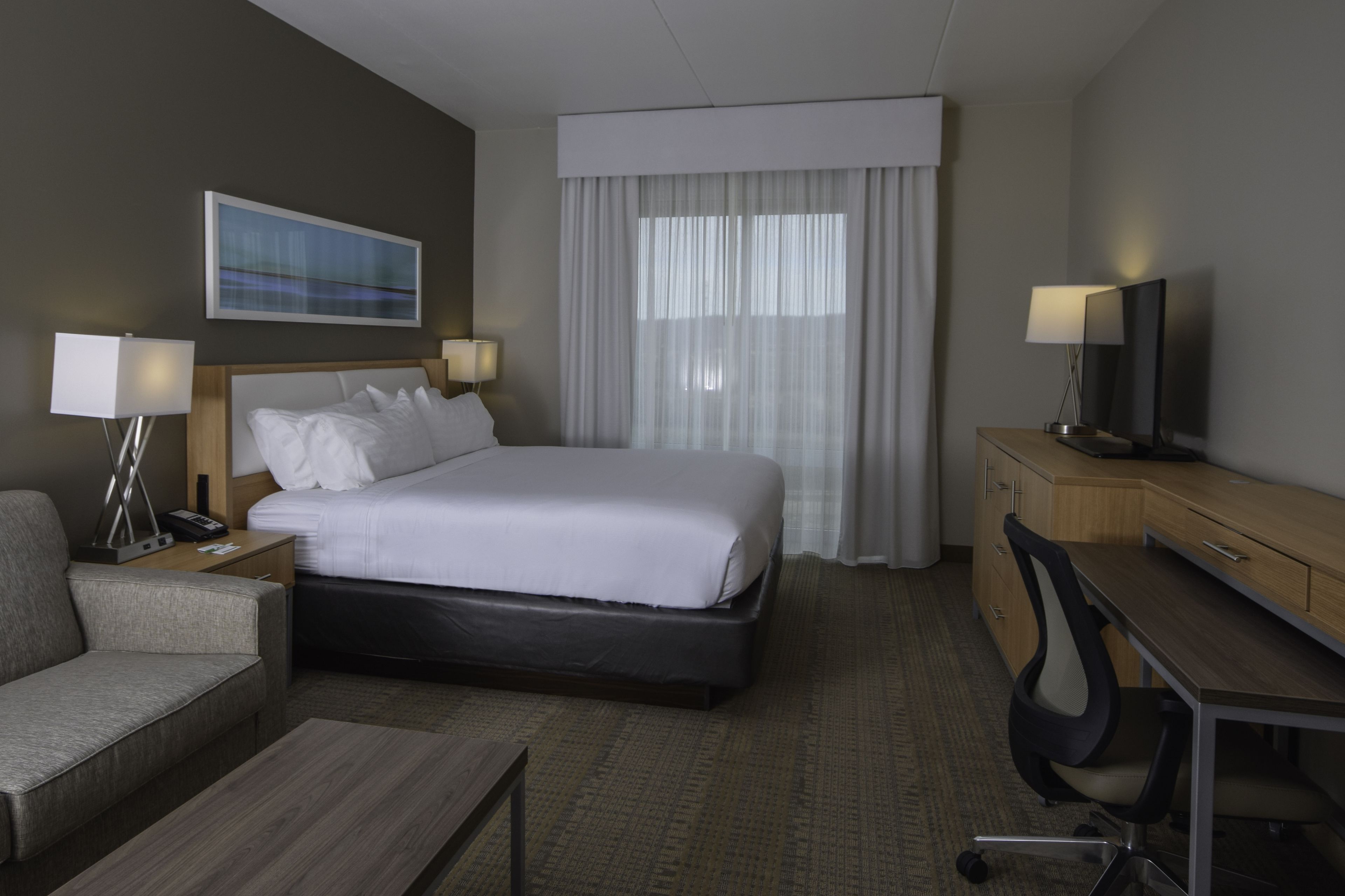 A hotel room with a bed, bedside tables, a desk, a chair, and a television.