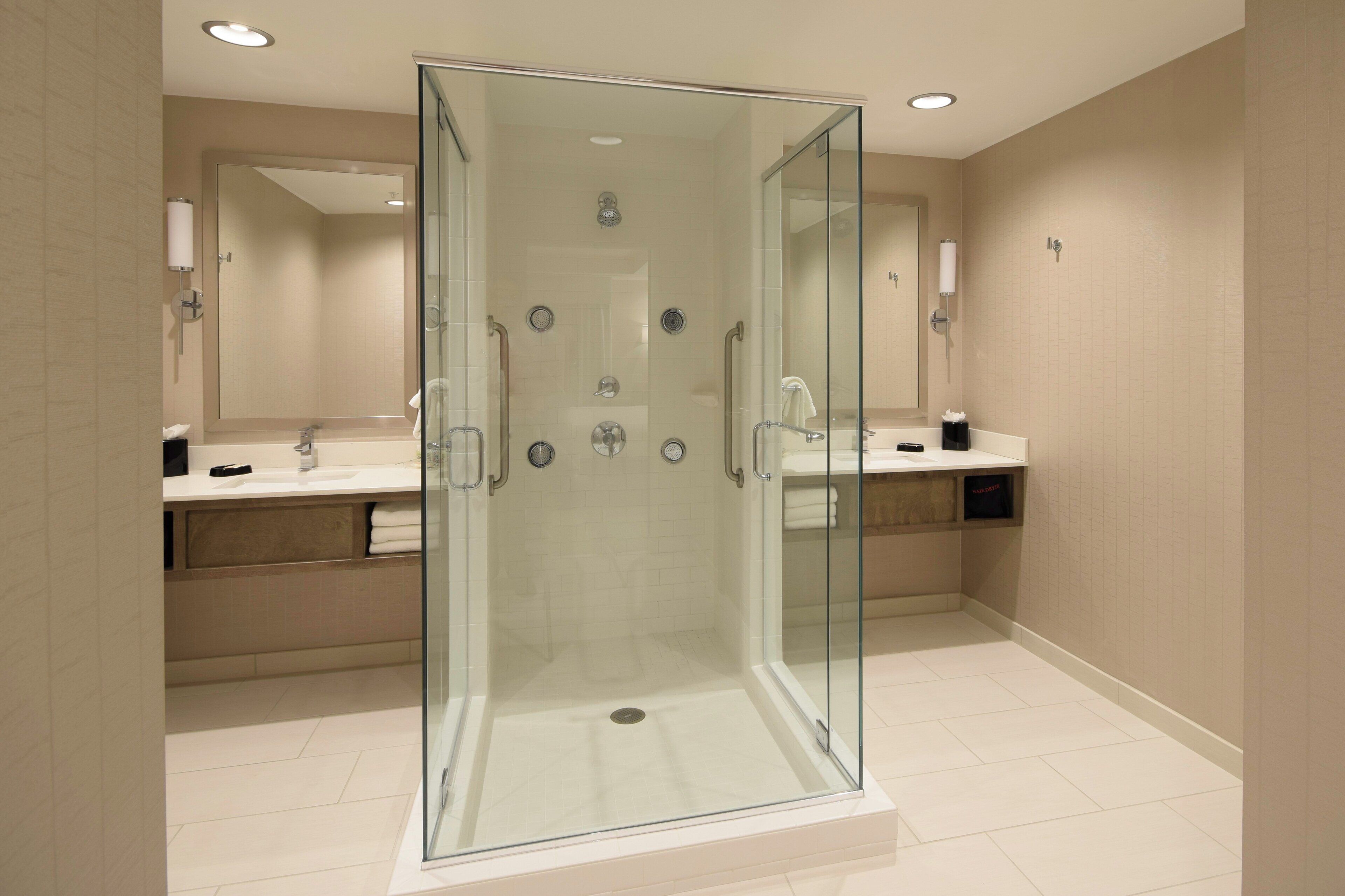 A modern bathroom with a glass-enclosed shower, two sinks, and a mirror.