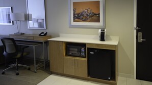 A compact hotel room with a kitchenette, a desk with a lamp, a chair, and a microwave. - Holiday Inn Cincinnati N - West Chester by IHG (West Chester)