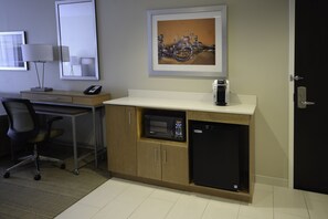 A compact hotel room with a kitchenette, a desk with a lamp, a chair, and a microwave. - Holiday Inn Cincinnati N - West Chester by IHG (West Chester)