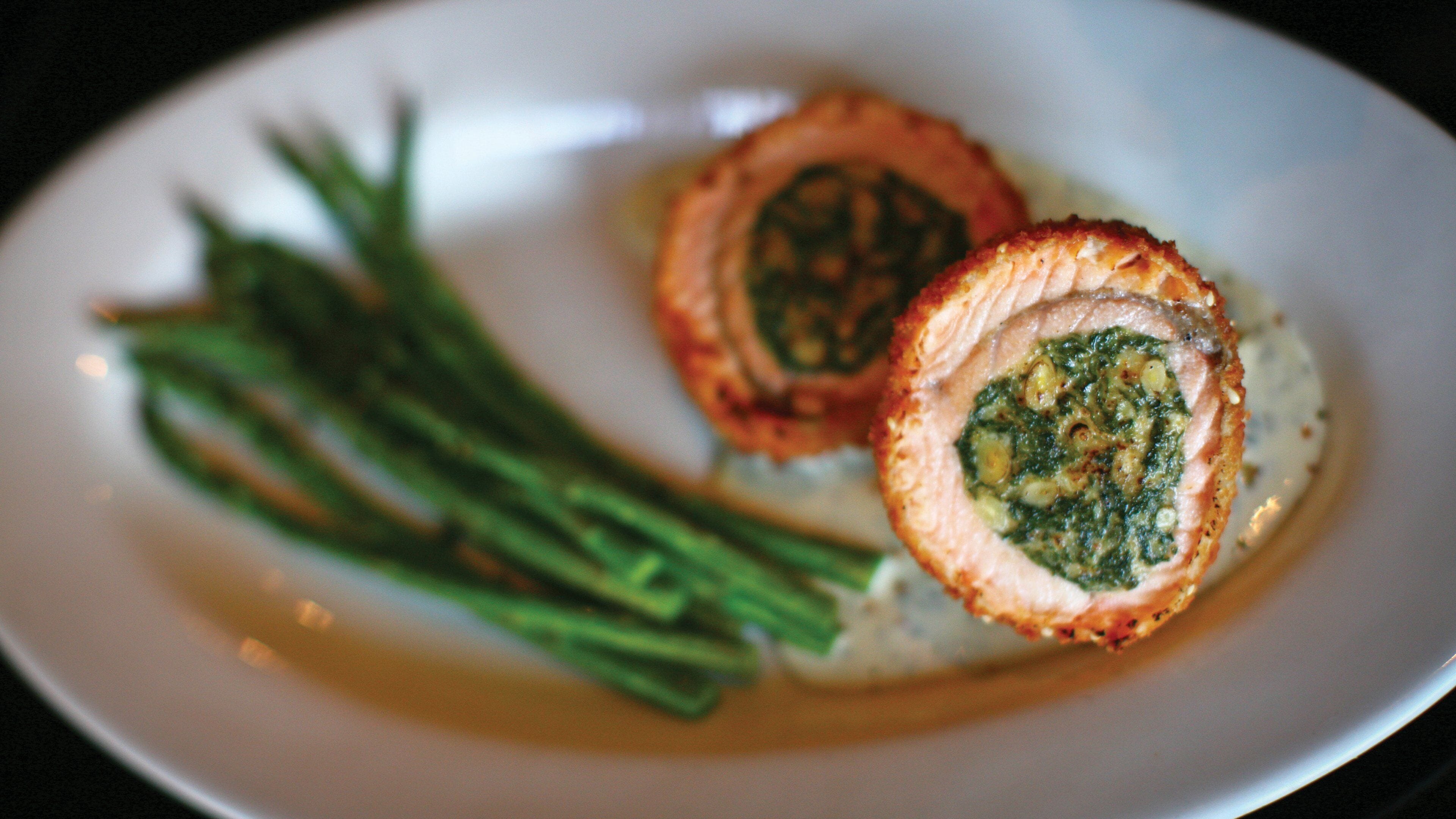 A plate with a rolled meat dish and green beans.