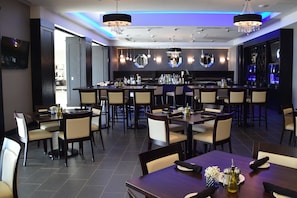 A modern dining area with multiple tables and chairs, a bar area with a counter, and decorative lighting fixtures. - Holiday Inn Cincinnati N - West Chester by IHG (West Chester)