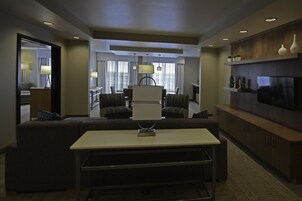 Quarto de hotel moderno com área de estar, mesa de jantar e televisão.
