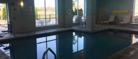 An indoor swimming pool with clear windows, a lifeguard chair, and a pool lift.