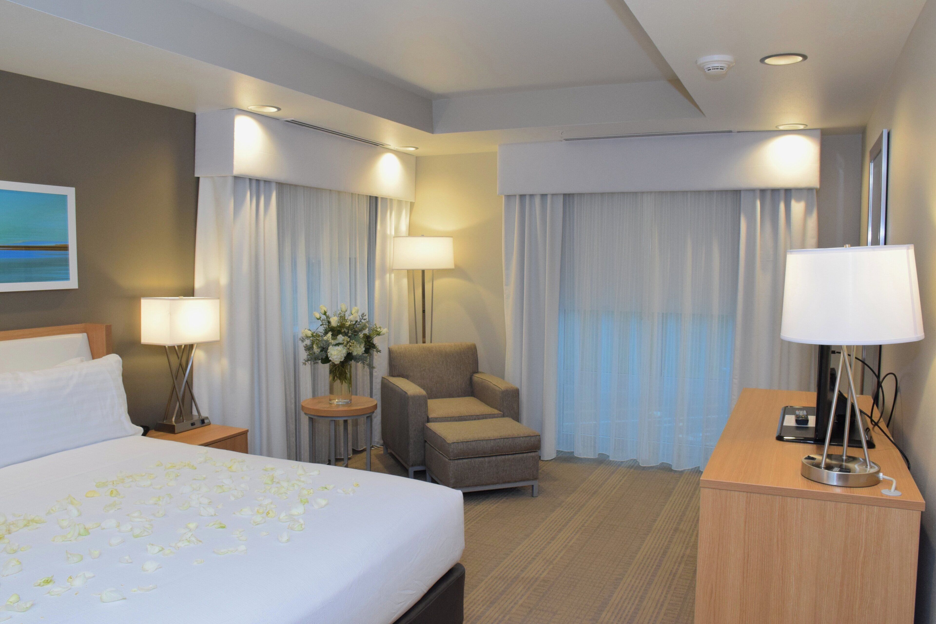 Quarto de hotel com cama, cadeira, escrivaninha e luminária.