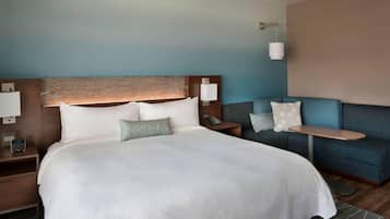 Una habitación de hotel con una cama grande, un sofá, una mesita de noche con lámpara y un teléfono instalado en la pared.
