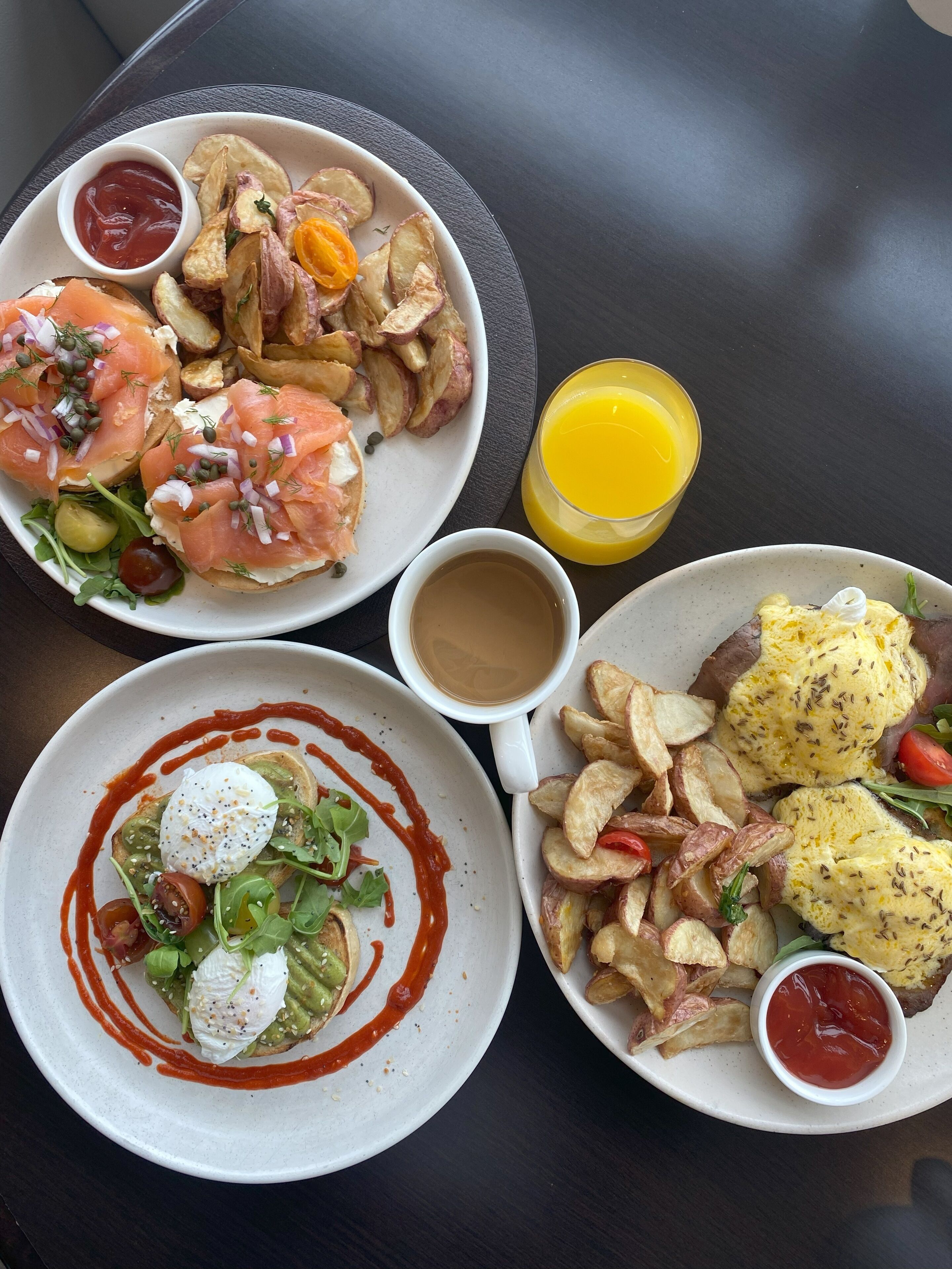 Une table avec trois assiettes de nourriture, un verre de jus d’orange et une tasse de café.