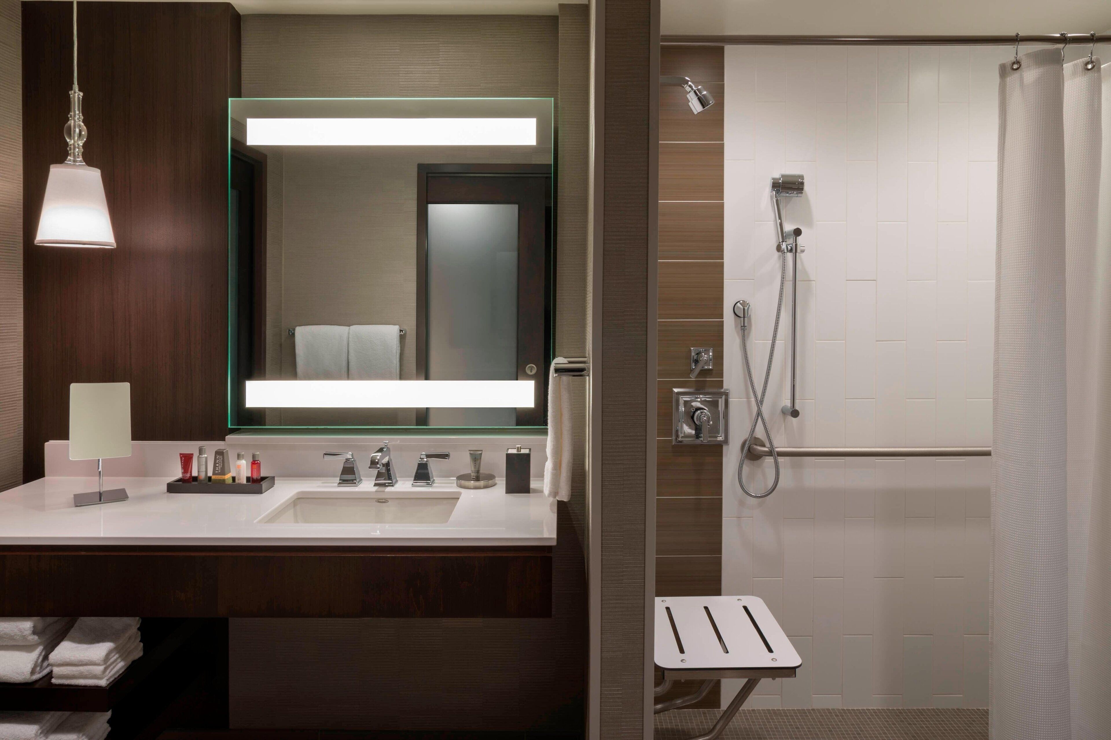 A modern bathroom with a double sink, a large mirror, a shower with a handheld showerhead, and a towel rack.