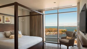 Un dormitorio amplio con una cama grande, un sillón cómodo y vistas a una masa de agua a través de ventanales.