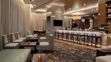 A modern hotel lobby with seating areas, a bar, and a television.