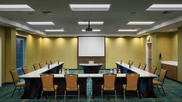 Una sala de conferencias con una larga mesa, sillas, una pantalla de proyector y piso alfombrado.