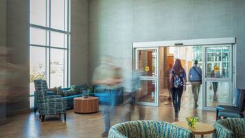 A spacious lobby with a large window, a blue sofa, patterned armchairs, and a glass door entrance.