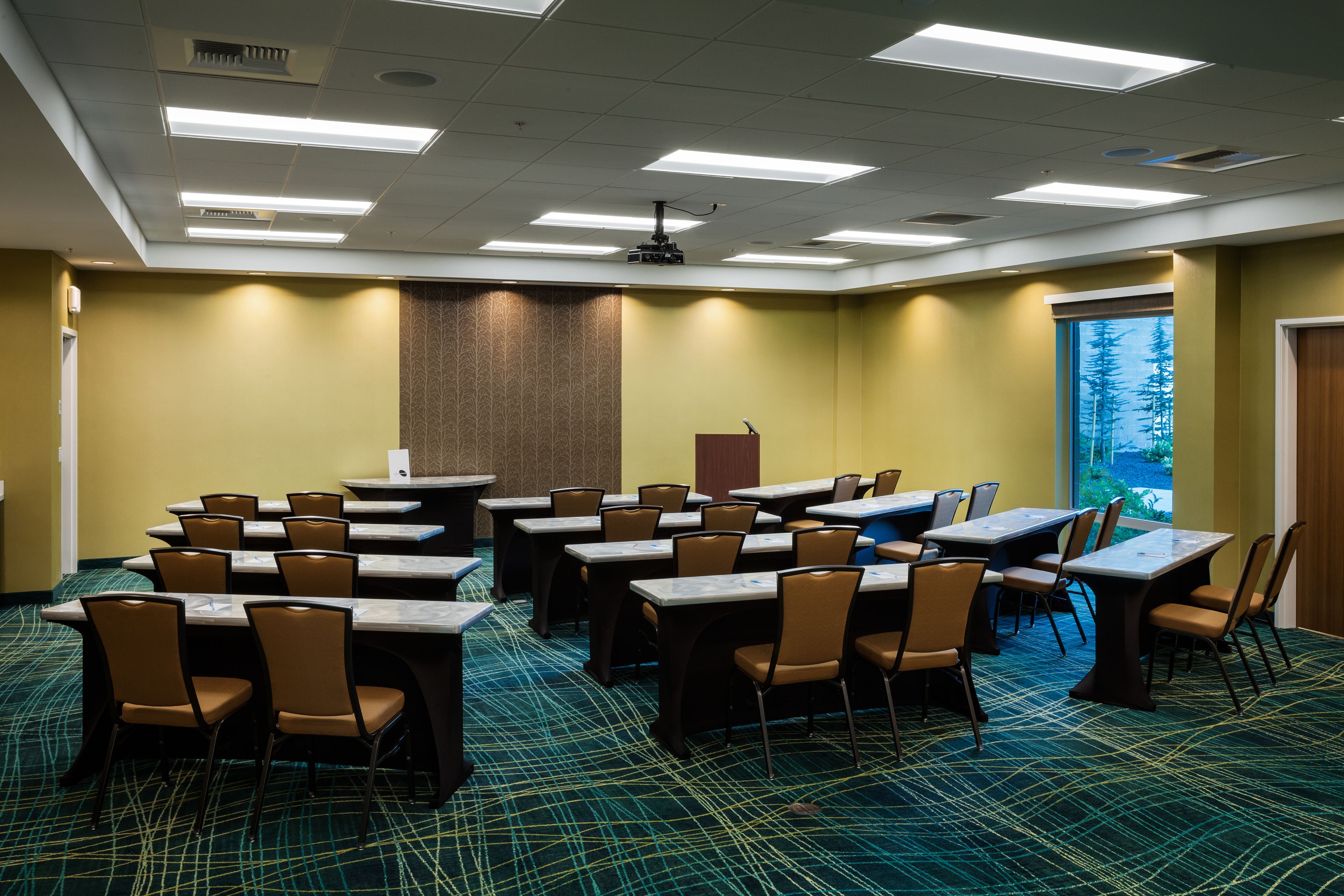 A conference room with tables and chairs, a podium, and a projector on the ceiling.