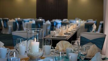 A banquet table set for a formal event with a lit candle centerpiece, white tableware, and teal chair covers.