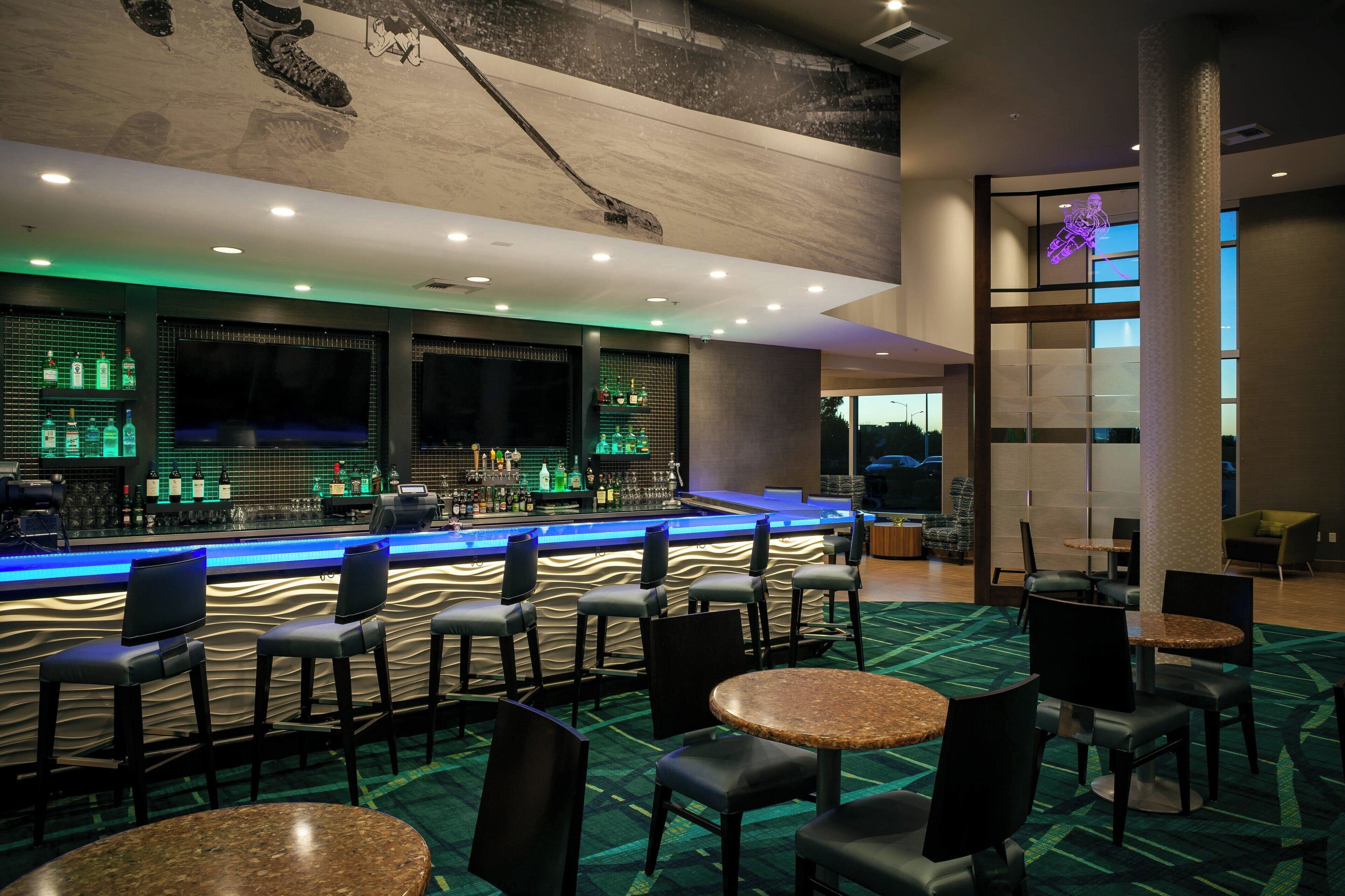 Un espace bar comprenant un comptoir, des tabourets de bar et un coin salon avec des tables et des chaises rondes.