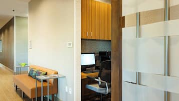 A modern hotel room with a sofa, a desk with a computer, and a kitchenette area.