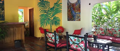 Una habitación con piso de baldosas, un banco de madera, sillas rojas, una pequeña mesa y una puerta que da a otra estancia.