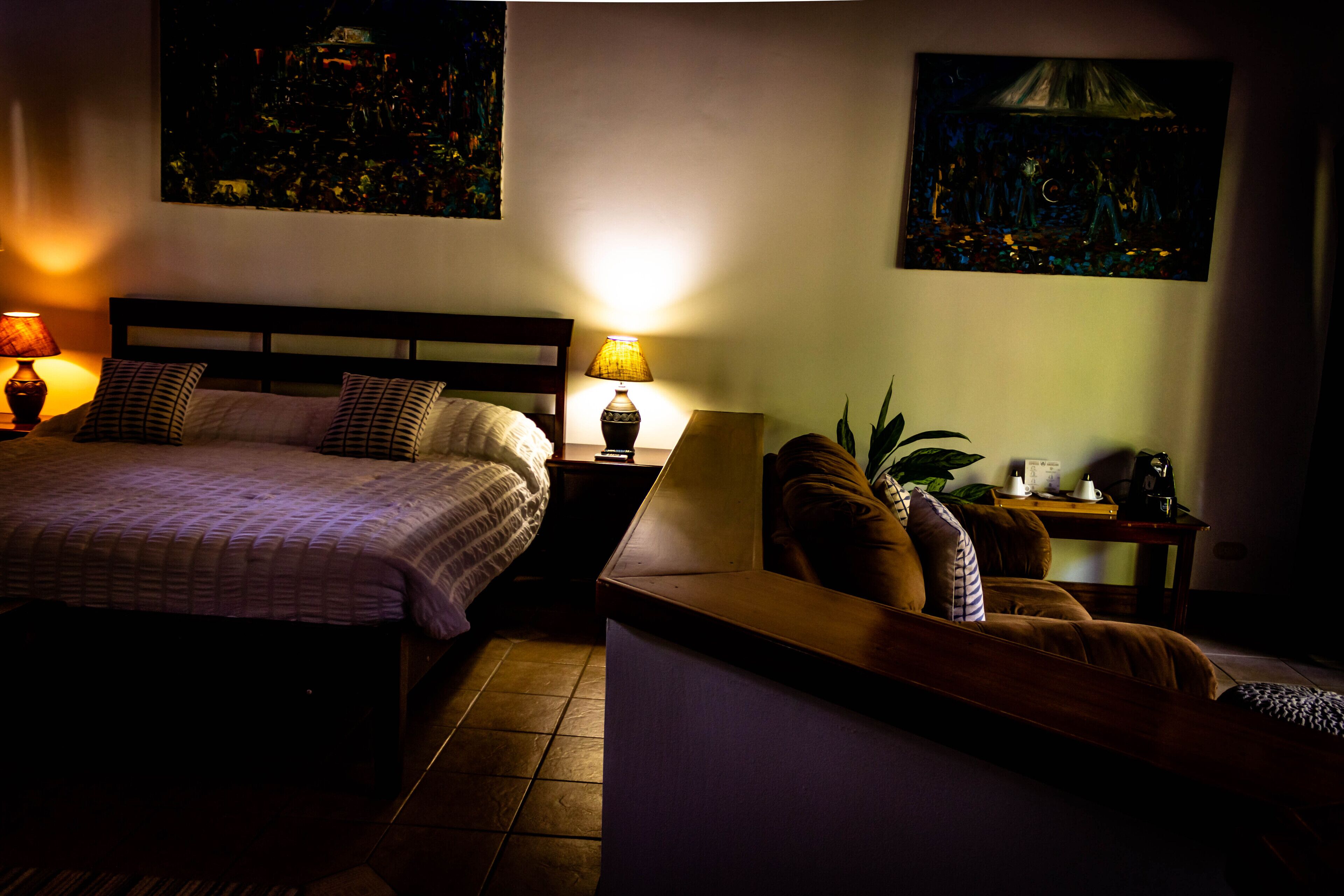 Une chambre d’hôtel avec un lit, des tables de chevet, un canapé et deux tableaux accrochés aux murs.