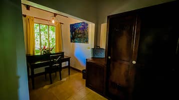 A room with a dining table, chairs, a window with curtains, a painting on the wall, and a door.