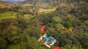 Ein Resort mit Schwimmbad, umgeben von üppiger Vegetation und Hügeln im Hintergrund.
