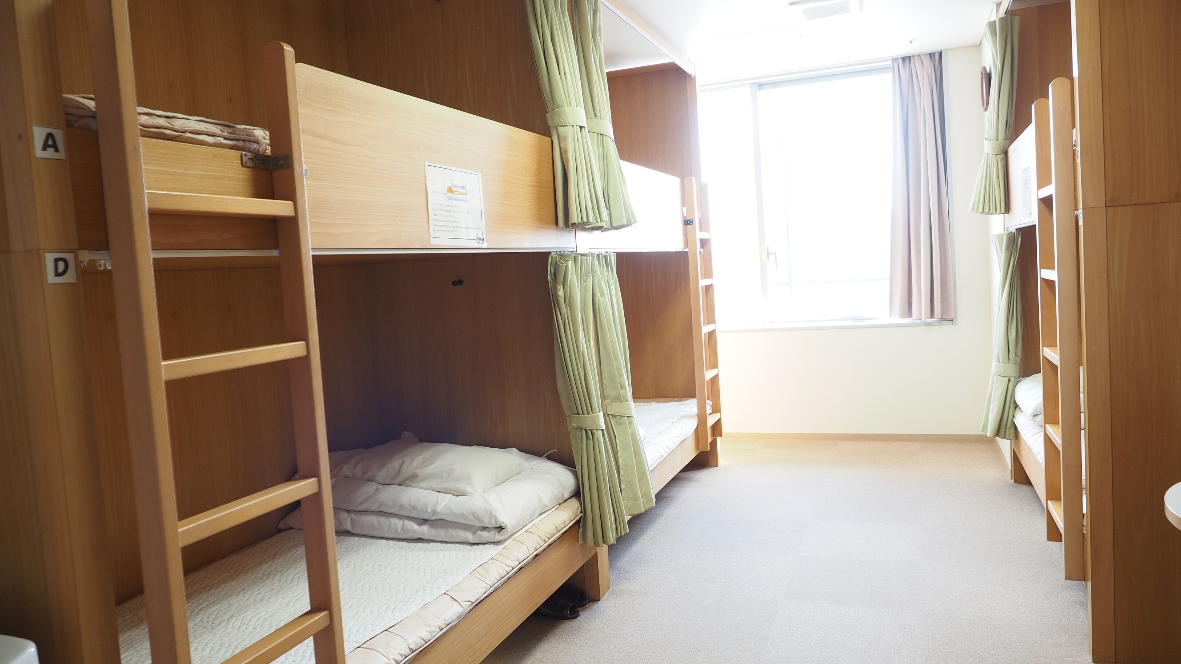 Quarto com beliche, janela, cortinas e um aviso na parede.