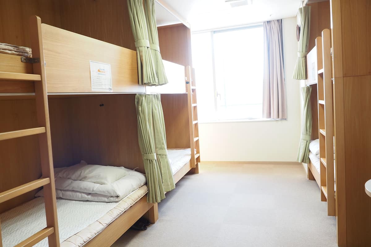 Une chambre avec un lit superposé, une fenêtre, des rideaux et un panneau accroché au mur.