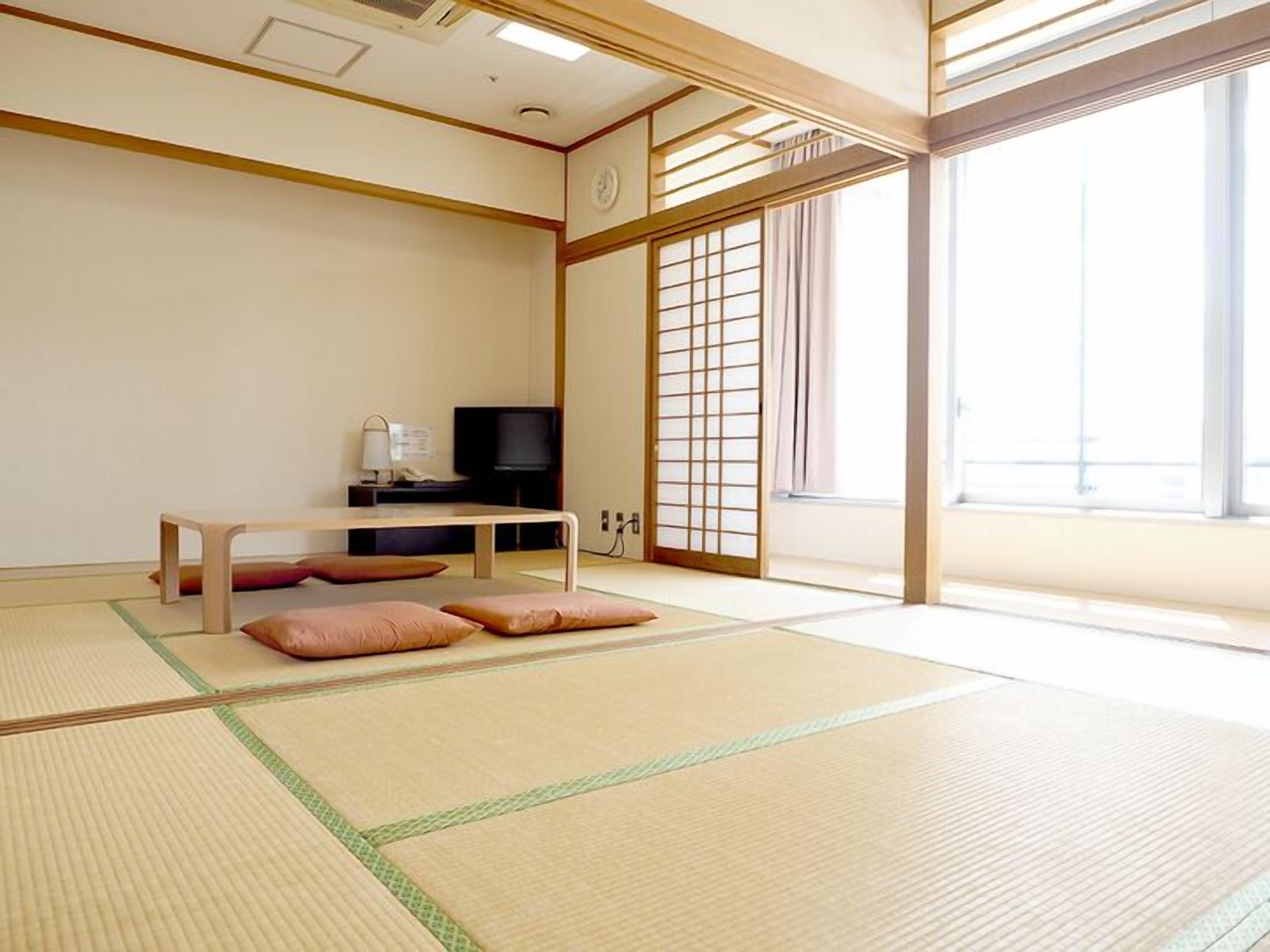 Una habitación con suelo de tatami, una cama futón, un televisor y una puerta corredera.