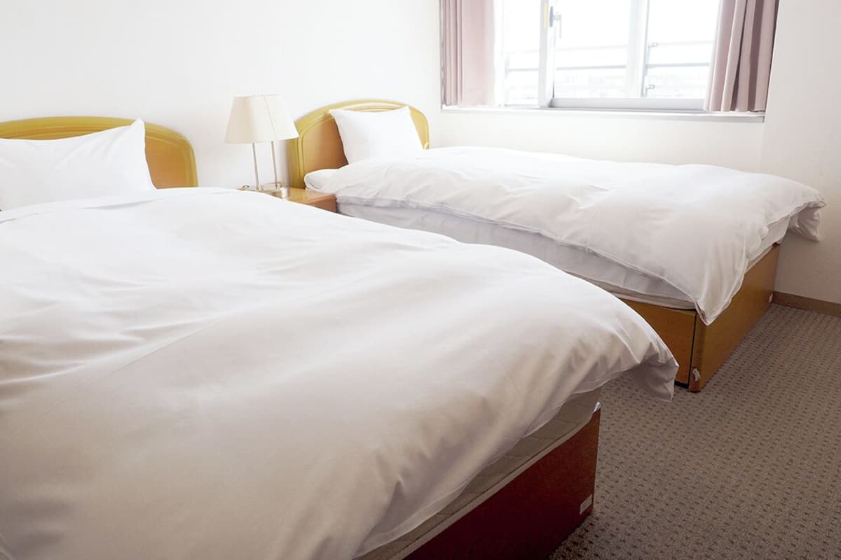Une chambre d’hôtel avec deux lits, une table de chevet avec une lampe et une fenêtre avec des rideaux.